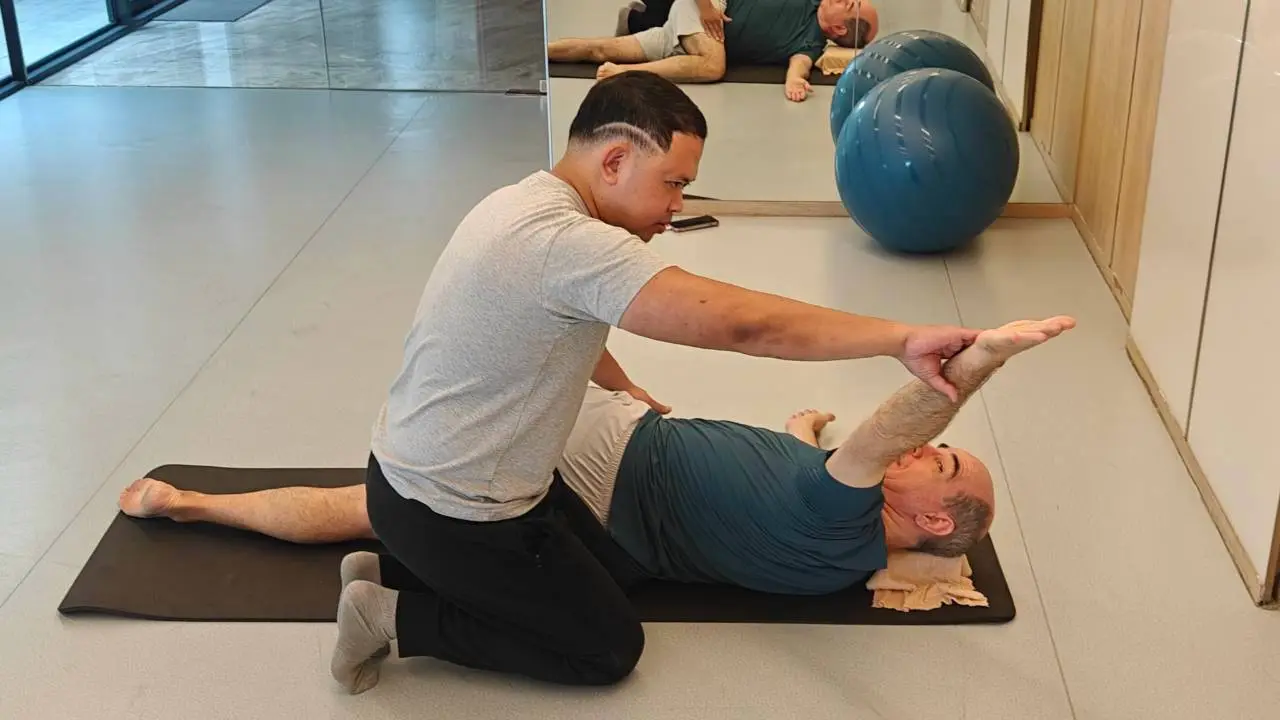 Boss kneeling beside a client, guiding a gentle floor stretch in a bright studio