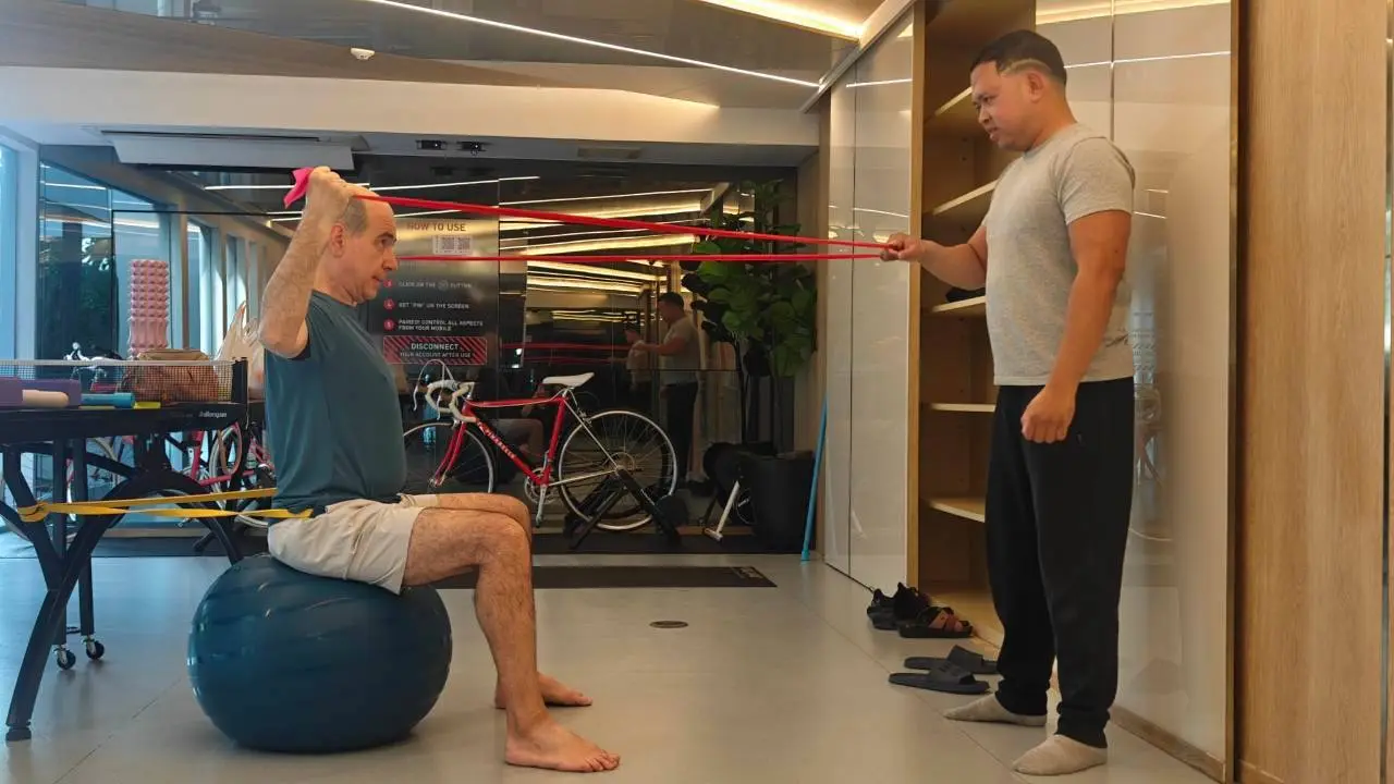 Client seated on a stability ball pulling a band overhead to free the neck and shoulders