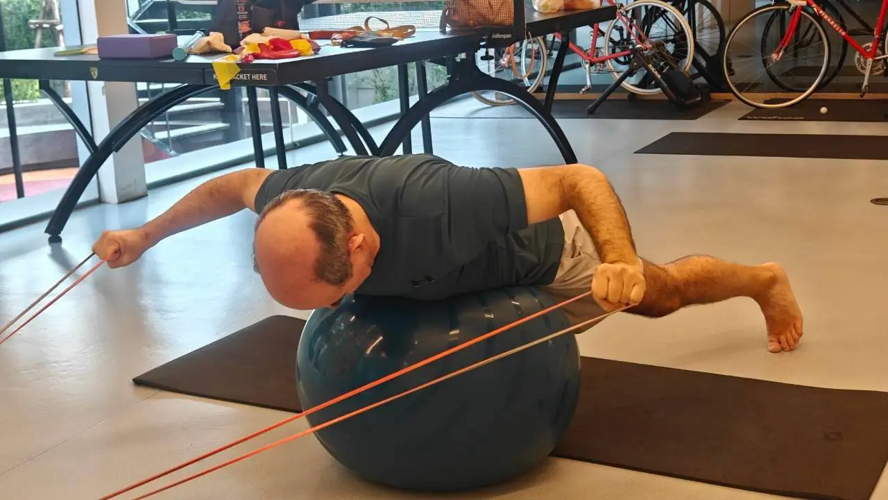 Client rotating with a resistance band over a stability ball for return-to-sport strength